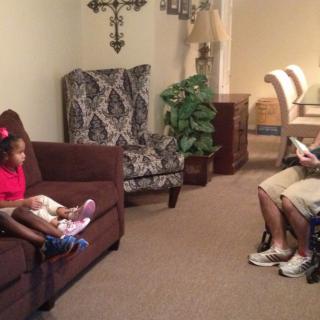 A man and child in a living room, with the man reading and the child sitting on a sofa.