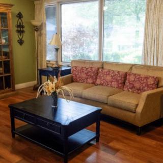 A cozy living room with a sofa and coffee table, featuring large windows and a hardwood floor.