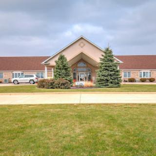 A welcoming entrance to a facility surrounded by neatly manicured lawns and trees under a cloudy sky.