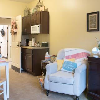 A cozy living room featuring an armchair with a colorful blanket and cushion, alongside a small cabinet.