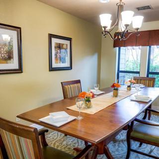 A cozy dining room with a wooden table set for a meal, adorned with flowers and illuminated by a chandelier.