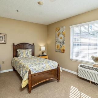 A cozy bedroom with a single bed, floral bedding, and natural lighting from a large window.