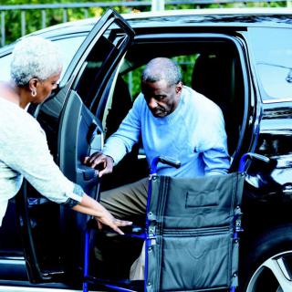 An elderly person is being assisted out of a car into a wheelchair.