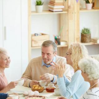 A group of seniors engaged in conversation around a table with tea.