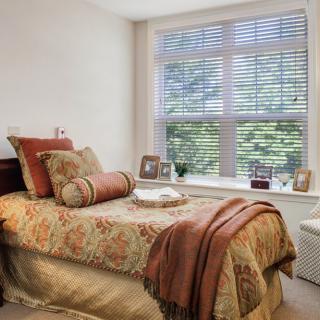 A cozy bedroom with a bed adorned with decorative pillows and a patterned blanket, featuring a large window letting in natural light.