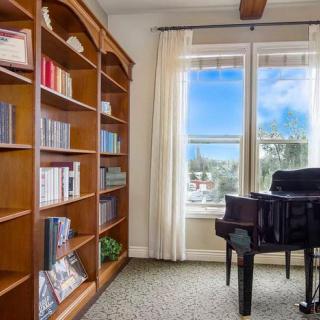 A cozy room featuring a wooden bookshelf and a piano near a large window.