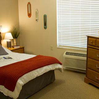 A cozy bedroom with a neatly made bed, wooden dresser, and warm lighting.