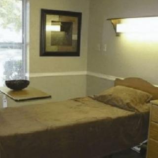 A minimalist bedroom featuring a single bed with brown bedding, a window, and simple decor.