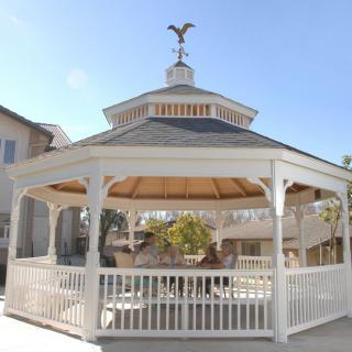 A wooden gazebo in an outdoor setting, featuring a peaked roof and open sides.