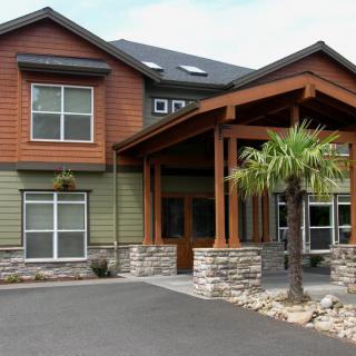 A modern residential house with a wooden porch and surrounding landscaping.
