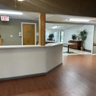 A spacious reception area with a wooden floor, featuring a front desk and decorative plants.
