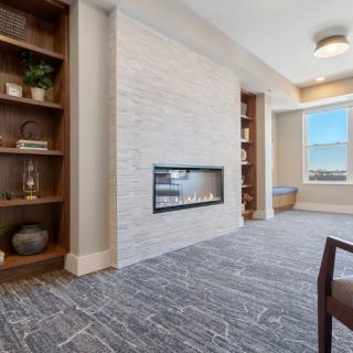 A modern living room with a white stone fireplace, built-in bookshelves, and large window.