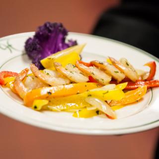 A gourmet dish featuring sliced shrimp and colorful bell peppers, garnished with a lemon wedge and purple cauliflower.
