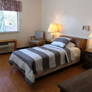 A cozy bedroom with a single bed featuring striped bedding, illuminated by a bedside lamp, and a window providing natural light.