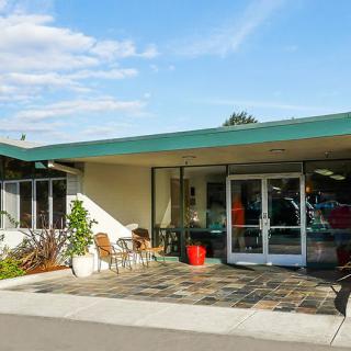 A mid-century modern motel exterior with a green roof and outdoor seating area.