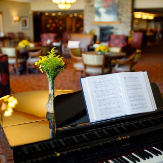 A cozy lobby featuring a piano with an open music sheet and a vase of flowers.