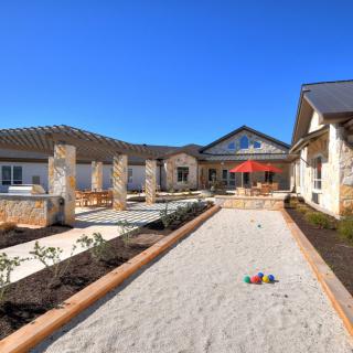 A sunny courtyard with a patio area surrounded by buildings and landscaping.