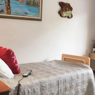 A simple bedroom featuring a single bed with a pillow and remote control, adorned by a painting on the wall.