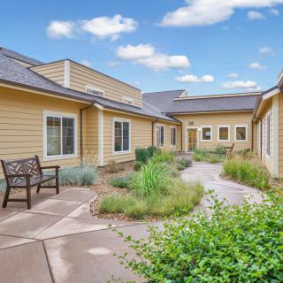 A peaceful courtyard with a bench surrounded by greenery and modern building exteriors under a partly cloudy sky.