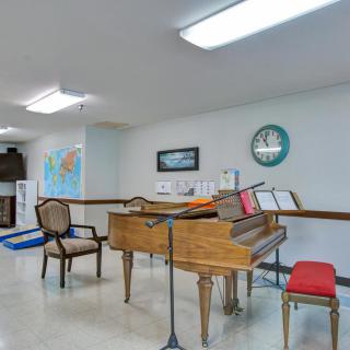A music room featuring a piano with sheet music, a chair, and various decorations including a map and clock on the wall.