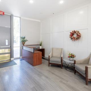 A reception area featuring a desk, two chairs, a wreath on the wall, and plants for decoration.