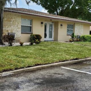 A suburban single-story house with a well-maintained lawn and adjacent parking lot.