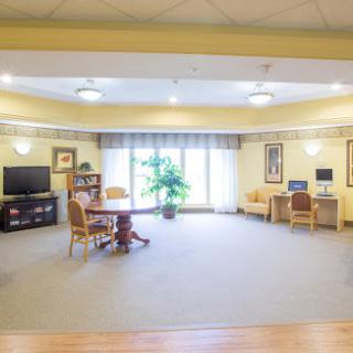 A spacious and bright common area featuring comfortable seating, a desk, and a television.