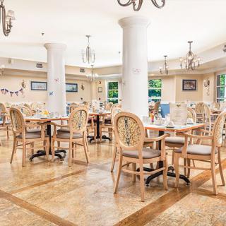 An elegant and empty restaurant interior featuring wooden tables and chairs with decorative chandeliers.