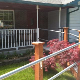 A cozy porch with a ramp and railings, surrounded by greenery and a small maple tree.