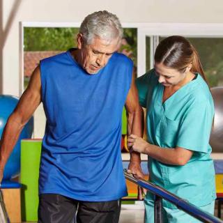 An elderly man receives assistance from a healthcare professional during a physical therapy session.