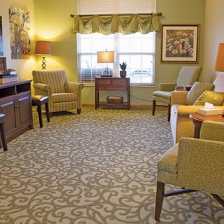 A cozy living room with patterned carpet, upholstered chairs, a sofa, and several lamps.