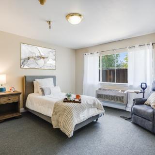 A cozy bedroom with a single bed, large window, and soft lighting.