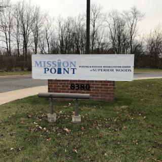 A sign for Mission Point, set against a backdrop of trees and grass.