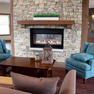 A cozy living room featuring a stone fireplace, wooden furniture, and comfortable armchairs.