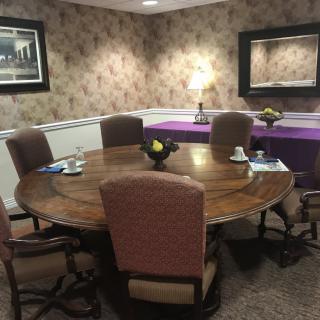 A cozy meeting room with a round wooden table surrounded by upholstered chairs, complemented by decorative wallpaper and soft lighting.
