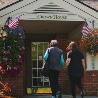 Two people walking towards the entrance of Crown House, adorned with flowers and flags.