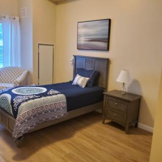 A cozy bedroom with a single bed, nightstand, and a window letting in natural light.
