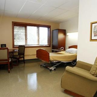 An empty hospital room with a bed, chair, and window.