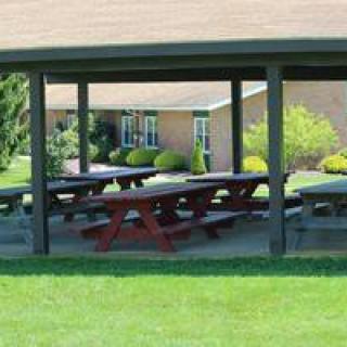 A covered picnic shelter with several tables situated in a grassy outdoor area near a building.