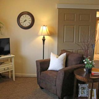 A cozy living room with a comfortable armchair, floor lamp, wall clock, and TV.