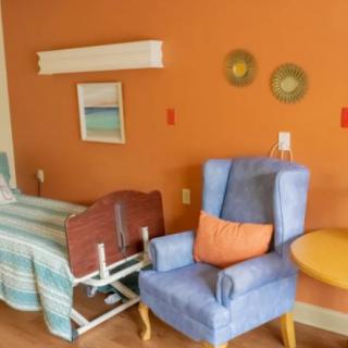 A cozy hospital room with an orange accent wall, featuring a bed and a comfortable armchair with a pillow.