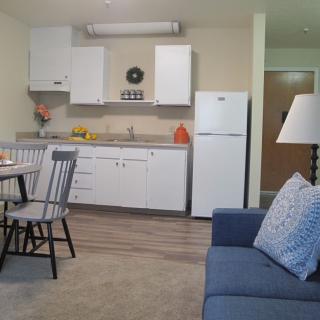 A cozy kitchen and living area featuring a dining table, chairs, refrigerator, and a comfortable sofa.