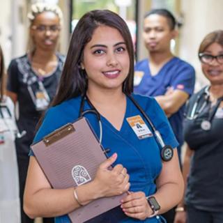 A nurse stands in a hospital corridor with her colleagues, holding a clipboard.