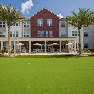 A modern residential building with a well-manicured lawn and palm trees under a clear blue sky.