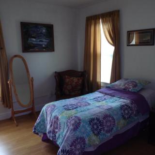 A cozy bedroom with a single bed, adorned with a colorful quilt, next to a window with brown curtains.