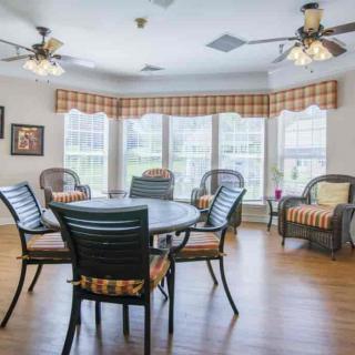 A cozy living and dining area featuring a round table with chairs, wicker furniture, large windows, and ceiling fans.