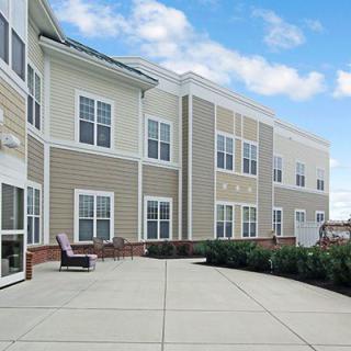 A modern residential building with a large, open patio area under a cloudy sky.