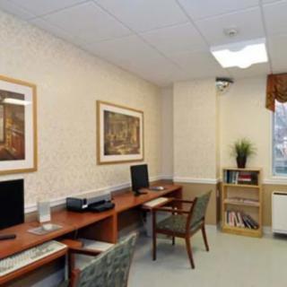 A small office workspace featuring computers, desks, and chairs with decorative paintings on the walls.