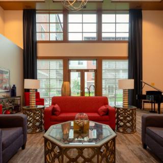 A stylish living room featuring a red sofa, modern coffee table, and a piano, with large windows allowing natural light to fill the space.