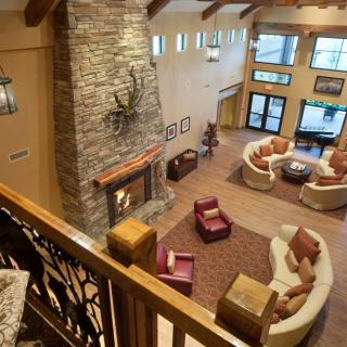 A cozy living room featuring a large stone fireplace, comfortable seating areas, and wooden beams overhead.